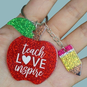 Detail of red glitter apple keychain with teach love inspire text and pencil charm