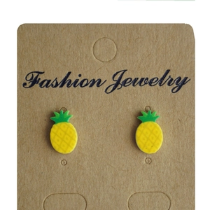 Detail shot of pineapple stud earrings in yellow and green on a kraft display card