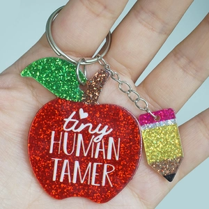 Close-up of glitter apple teacher keychain with Tiny Human Tamer text held in hand