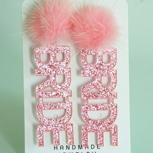 Nahaufnahme der rosa glitzernden BRIDE Ohrringe mit Pompons für die Hochzeit