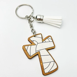 Detail of wooden cross keychain with white tassel and silver ring on white background