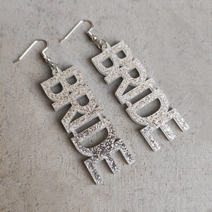 Makro-Detail der silbernen Glitzer BRIDE Buchstaben-Ohrringe für Brautparty-Accessoires