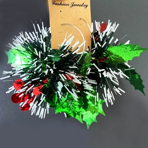 Close-up of Christmas earrings with green holly leaves and festive red ribbons