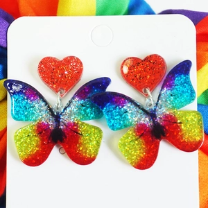 Detailed close-up of butterfly earrings with vibrant rainbow glitter and red heart studs