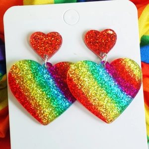 Macro detail of rainbow glitter acrylic heart earrings on a striped fabric background