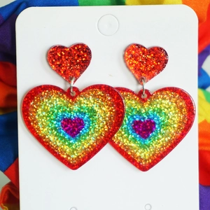 Close-up of rainbow glitter heart dangle earrings on a white display card with stripes