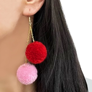 Close-up of pink and red fuzzy pompom drop earrings hanging on a gold chain link