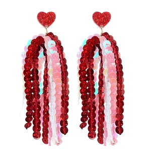 Détail de boucles d'oreilles cœur pailleté avec glands de sequins rouges et roses superposés