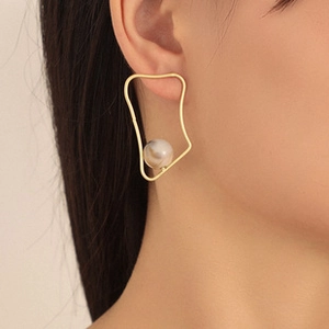 Dettaglio di un orecchino geometrico dorato minimalista con grande perla color crema