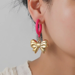 Detail of fuchsia matte hoop earrings with golden bow pendants worn on the ear