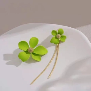 Detail of neon green flower earrings with gold chain tassels on a white display tray