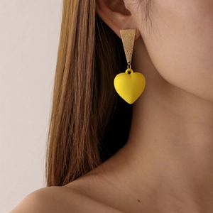 Macro view of matte yellow heart drop earrings featuring a gold geometric stud on a model