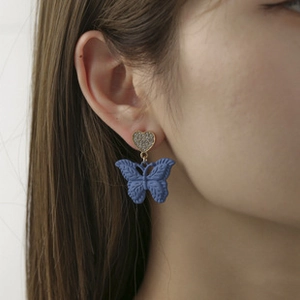 Dettaglio di un orecchino a farfalla blu opaco con perno a cuore glitterato su una modella
