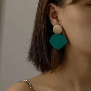 Close-up of geometric matte gold round and dark green rhombus earrings on model