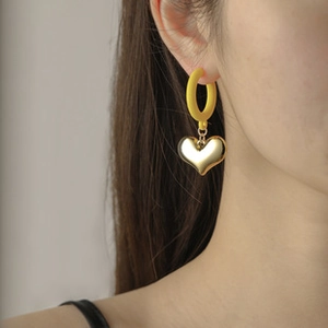 Detail of a matte yellow hoop earring with a mirror-finish gold heart pendant on model