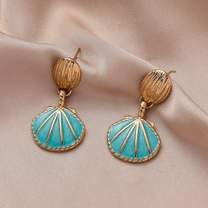 Detail of drop shell earrings with teal enamel and textured gold disc on silk fabric