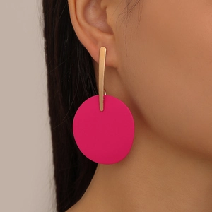 Close-up of geometric earrings with gold bars and large matte pink round lacquer charms