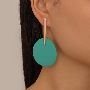 Close-up of a model wearing large geometric earrings with gold bars and green matte drops