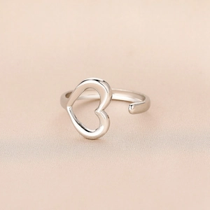 Macro detail of silver open heart ring showing polished finish on beige silk background