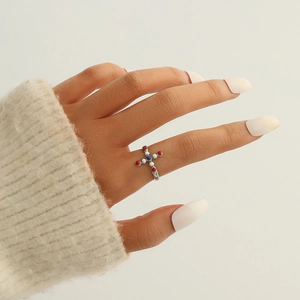 Détail d'une bague croix en argent avec émail coloré portée au doigt sur fond de tricot