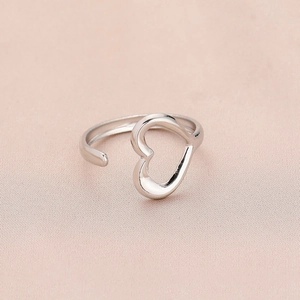 Minimalist adjustable open heart ring in silver finish on soft pink textured background