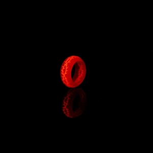 Gros plan d'une bague lumineuse en résine rouge avec motifs épines sur fond sombre