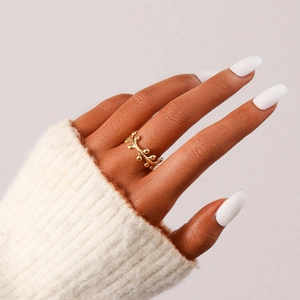 Goldener Edelstahlring im Ranken-Design getragen mit weißem Strickpullover