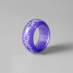 Gros plan d'une bague en résine violette avec motif d'épines blanches au style gothique
