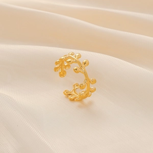 Nahaufnahme des goldenen Zweigrings mit Rankendesign auf beigem Seidenstoff-Hintergrund
