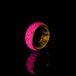 Leuchtring mit pinker Struktur-Außenseite und goldenem Innenband auf Spiegeloberfläche