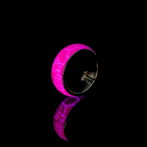 Anello luminoso con trama a coccodrillo rosa mostrato su una superficie riflettente