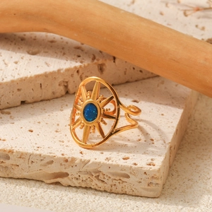 Golden sunburst open ring with oval blue gem on natural stone background