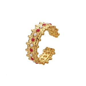 Détail d'une bague ouverte dorée avec points en émail rouge et blanc et bord perlé