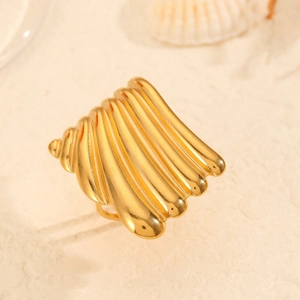 Anello regolabile a conchiglia dorata con trama a onde su sfondo di sabbia