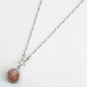 Detailed macro of stainless steel bead chain and round religious pendant with red inlay
