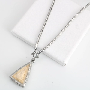 Gros plan sur une chaîne tressée argentée avec un pendentif religieux gravé triangulaire