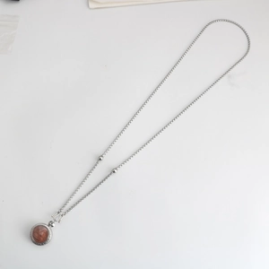 Detail van zilveren kralenketting met S-haaksluiting en ronde roodbruine hanger op wit
