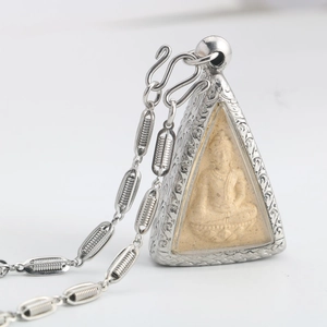 Detailed close-up of Thai Buddha amulet with silver-toned floral engraved metal frame