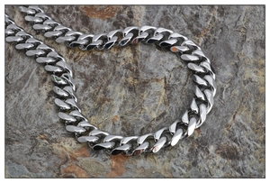 Macro shot of polished silver curb chain necklace on a rugged stone background
