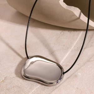 Minimalist silver irregular pendant necklace with black cord on stone background