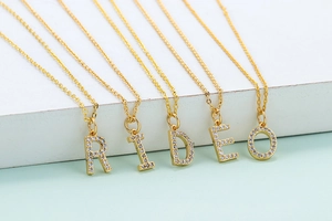 Detail of five gold letter necklaces with zircon inlays on a white display stand