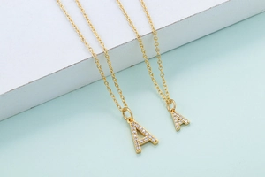 Detail of two gold letter A necklaces with sparkling white zircon stones on green base