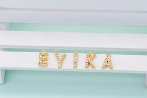 Macro shot of gold letter pendants E, Y, I, K, A with white zircon inlay on white stand