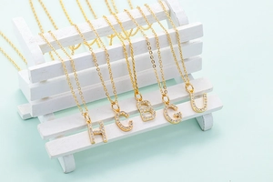 Close-up of gold initial necklaces with sparkling cubic zirconia on a white miniature bench