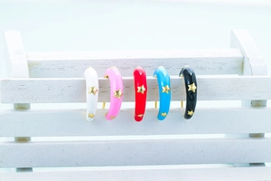 Détail de cinq boucles d'oreilles étoiles en émail blanc, rose, rouge, bleu et noir