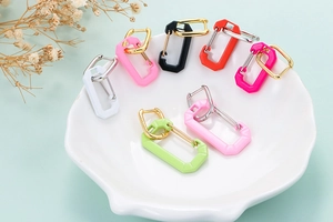 Colorful carabiner hoop earrings in enamel finish arranged on a white shell tray