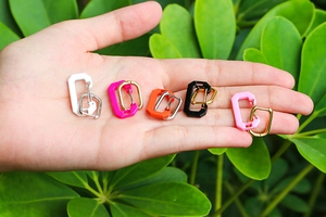 Close-up of hand holding colorful geometric carabiner earrings in outdoor natural lighting