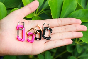 Macro shot of hot pink and black carabiner-style earrings held in palm for scale
