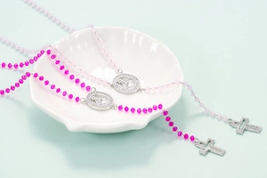 Close-up of Virgin Mary and cross necklaces with rose pink and light pink beads