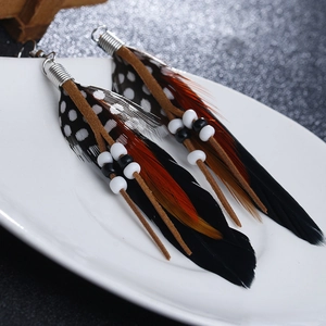 Detail of bohemian long feather earrings with seed beads and brown suede cord on ceramic tray
